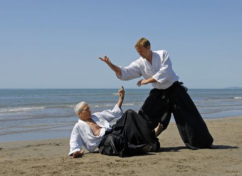 Two adults are training in Aikido on the beach