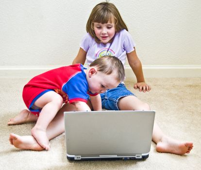 Little girl allows her baby brother to mess with the laptop computer.