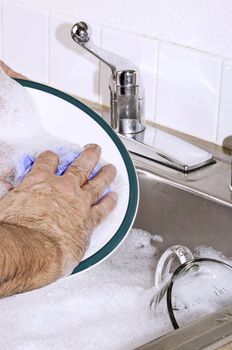Hand washing a dinner plate in the kitchen sink.