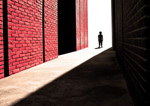 Processed photograph of a distant boy next to a brick wall. Used to illustrate a single child's strength, challenges and fear.   