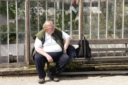 large man sitting on a bench infront of a greenhouse