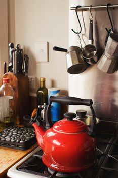 A red kettle sits on a stove with other kitchen utensils