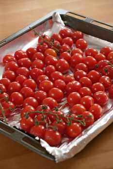 Group of oven roasted cherry tomatoes on foil and roasting pan. Shallow DOF with focus across middle.