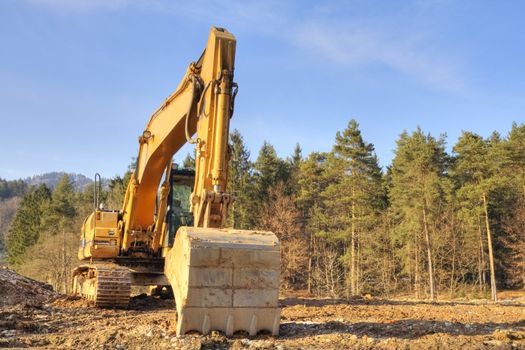 Yellow dredger on construction ground against forest and sky.