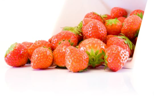 high key image of a collection of strawberries spilling from a white bowl on a white background