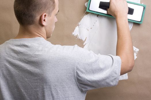 Caucasian worker plastering a brown wall with white plaster.