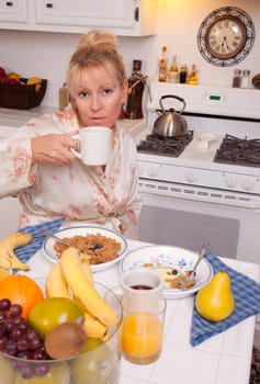 Attractive Woman In Kitchen with Fruit, Coffee, Orange Juice and Breakfast Bowls.