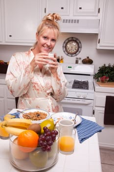 Attractive Woman In Kitchen with Fruit, Coffee, Orange Juice and Breakfast Bowls.