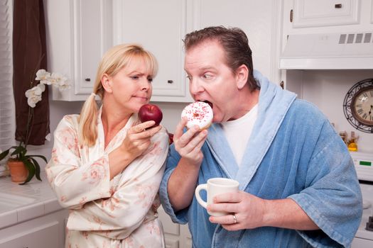 Couple in Kitchen Eating Donut and Coffee or Healthy Fruit.