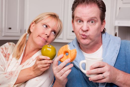 Couple in Kitchen Eating Donut and Coffee or Healthy Fruit.