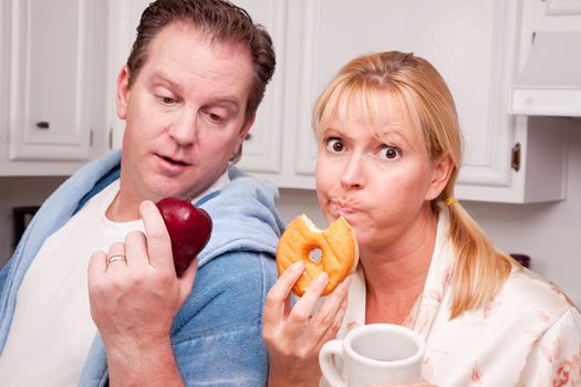 Couple in Kitchen Eating Donut and Coffee or Healthy Fruit.