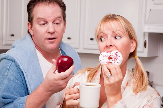 Couple in Kitchen Eating Donut and Coffee or Healthy Fruit.