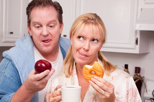 Couple in Kitchen Eating Donut and Coffee or Healthy Fruit.