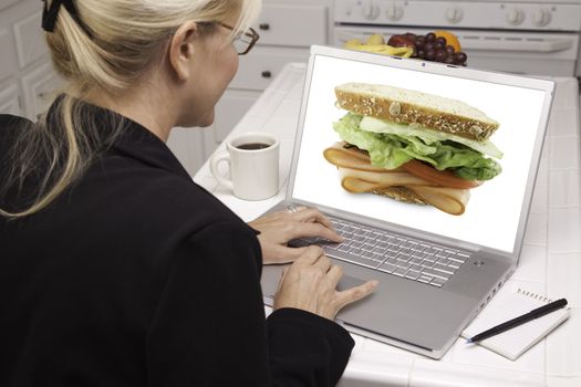 Woman In Kitchen Using Laptop to Research Cooking and Recipes. Screen can be easily used for your own message or picture. Picture on screen is my copyright as well.