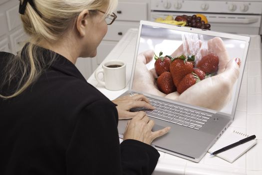 Woman In Kitchen Using Laptop to Research Cooking and Recipes. Screen can be easily used for your own message or picture. Picture on screen is my copyright as well.