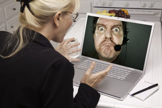 Shocked Woman In Kitchen Using Laptop with Grumpy Customer Support Man On Screen. Screen can be easily used for your own message or picture. Picture on screen is my copyright as well.