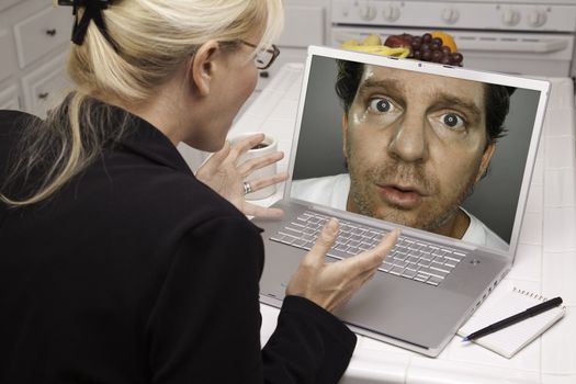 Shocked Woman In Kitchen Using Laptop with Strange Man on Screen. Screen can be easily used for your own message or picture. Picture on screen is my copyright as well.