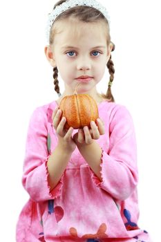Beautiful little girl holds a pumpkin up to the viewer.