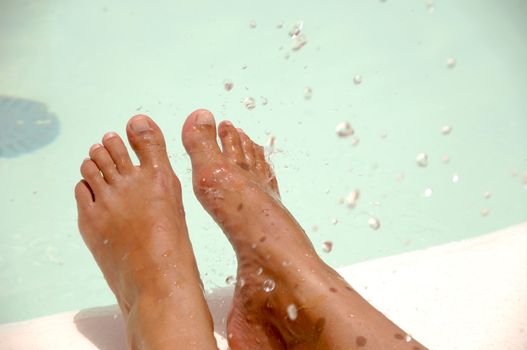 Feet by the pool side is being refreshed by cool water drops