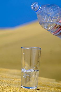 A glass of fresh water and bottle in a desert. Note that the water and bubbles are in motion blur.