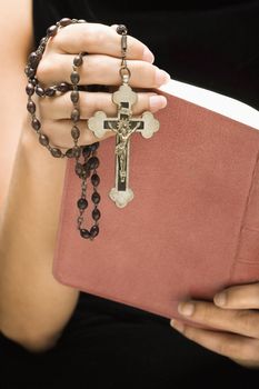 Woman holding Holy Bible open with rosary and crucifix in hand.