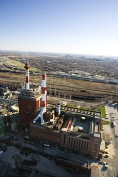 Aerial view of factory with smokestacks and city in distance.