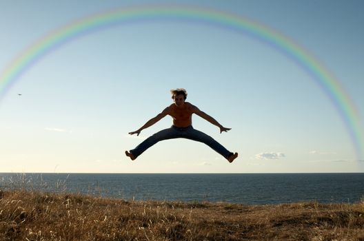 sporty man jumping under big colorful rainbow