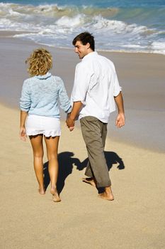 Attractive couple holding hands walking on beach smiling at eachother in Maui, Hawaii.