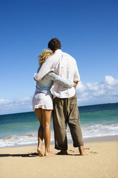 Attractive couple standing embracing looking out at ocean in Maui, Hawaii.