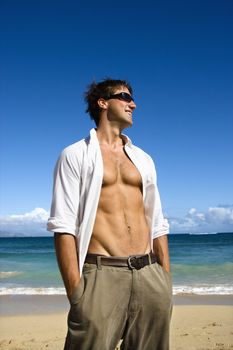 Portrait of attractive man standing with shirt unbuttoned wearing sunglasses on Maui, Hawaii beach.