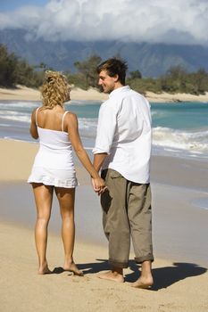 Attractive couple holding hands and smiling at eachother walking on Maui, Hawaii beach.