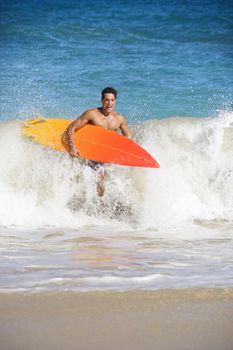 Attractive young man running out of water carrying surfboard in Maui, Hawaii.