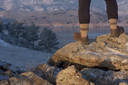 hiker or trail runner legs and feet on rock overlooking mountain lake,  winter scenery with snow, fog, frost at sunrise light in Colorado