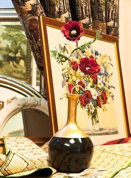 gobelin picture with red flowers in vase near it