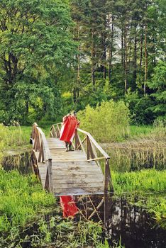 The fisher in a red raincoat on the wooden bridge leaving in water