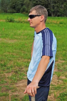 The young sportsman in dark glasses stand and keeps a hand on wooden column