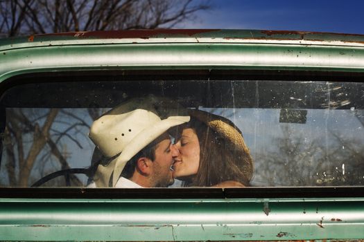 Cowboy and girlfriend kissing in through the back window of a pickup truck