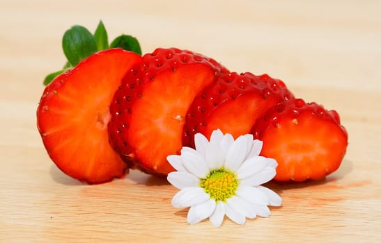 Slices of strawberry with camomile on a wood background
