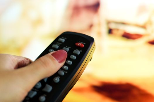 Hand holding remote control pointing to blurred TV program