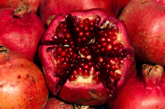 Closeup on several pomegranate fruits, the center one is cut in halves