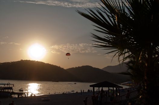 Great sunset in Oludeniz, near Fethiye, Turkey,with palm, beach hut, people, boat and parachutist