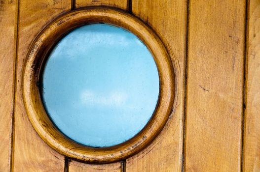 Porthole in old wooden ship's door with great blue sky visible through the glass