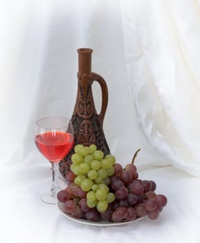 Bright still life with grapes and wine on white drape