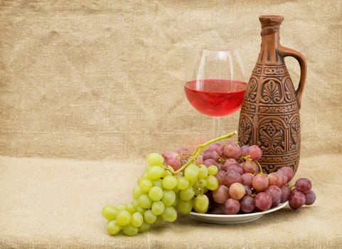 Ceramic brown bottle, grapes and red wine on sacking