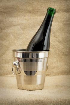Champagne bottle in metallic bucket on canvas background