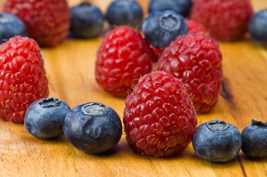 A couple of fresh ripe rasberry and blueberry on the wooden plate