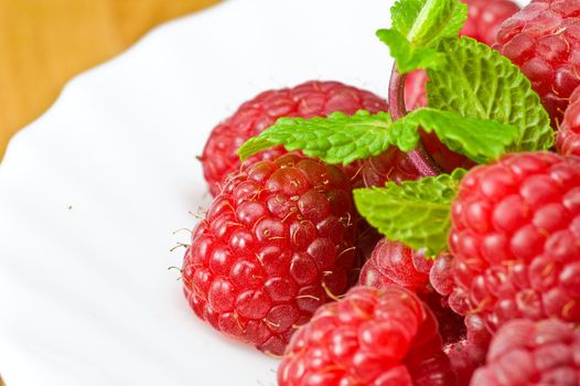 Fresh ripe rasberry and fresh mint leaves close-up on white porcelain plate