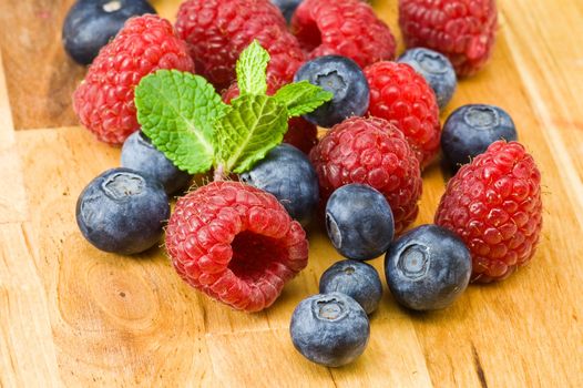 Fresh ripe raspberry and blueberry with green mint leaves on wooden plate