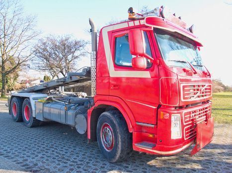 Front side view of red skip truck with hydraulic lifting  arm