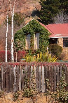 a quaint little sandstone house covered in lush autumn foliage with an old wooden hedge